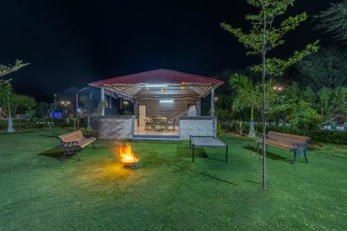 a fire in a yard with two benches and a building at ELIVAAS 5 BHK With Pvt Pool & Garden - Zenora in Gurgaon