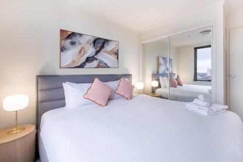 a bedroom with a large white bed with pink pillows at Stylish Cosy Gem w Pool, Tennis Court, & Parking in Melbourne