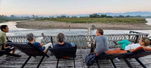 a group of people sitting in chairs by the water at Sapana Village Lodge in Sauraha