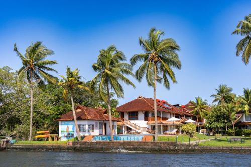 a house on the water with palm trees at Backwater Ripples Kumarakom in Kumarakom