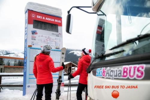 three people in red jackets holding skis next to a bus at Chata 107 Tatralandia Village in Liptovský Mikuláš