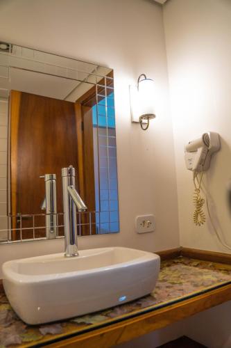 a sink in a bathroom with a large mirror at Hotel Ascona in Campos do Jordão