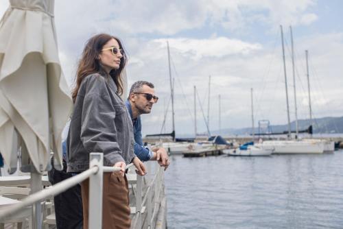 a man and a woman standing on a dock near the water at URBANAUTS STUDIOS Minelli in Trieste