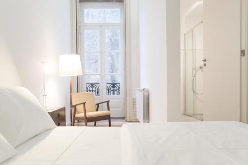 a white bedroom with a bed and a chair and a window at Republica Boutique Hostel in Porto