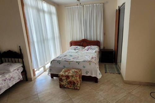 a bedroom with a bed and a ottoman in front of a window at Casa Aconchegante in Anchieta