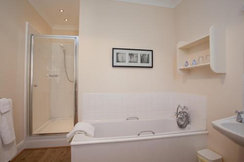La salle de bains blanche est pourvue d'une baignoire et d'une douche. dans l'établissement Skerrols House, à Bridgend