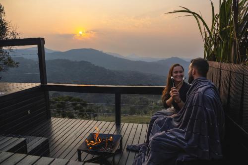 a man and a woman sitting on a deck with the sunset at Cabanas Duas Faces - Urubici in Urubici