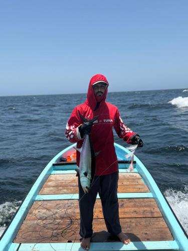 a man standing on a boat holding a fish at GUEST HOUSEs OYSTERS in Al Ḩadd