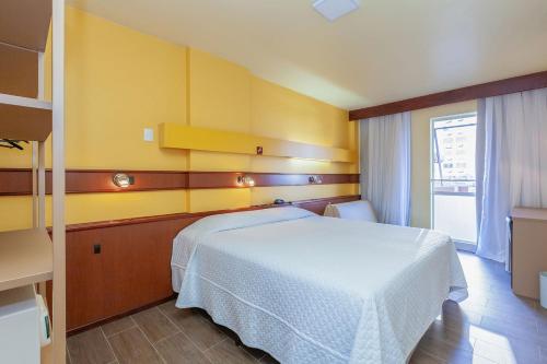 a bedroom with a white bed and a yellow wall at Tri Hotel Bento Gonçalves in Bento Gonçalves