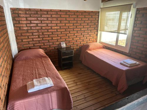 a room with two beds and a brick wall at Kaizen Apart Departamento 3 in Caleta Olivia