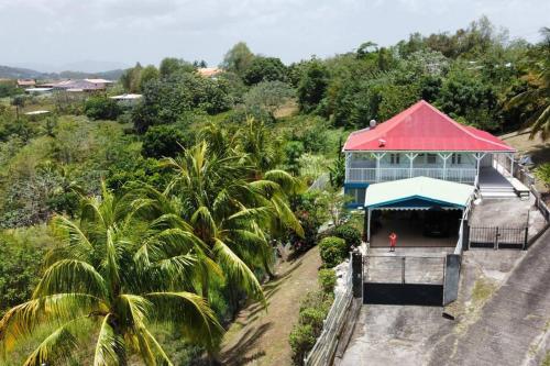 a building with a red roof next to palm trees at Haut de villa 1chambre climatisée à 3min de l'habitation Clément in Le François