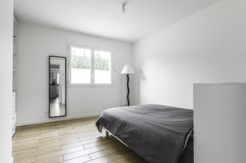 a white bedroom with a bed and a mirror at Appartement de 70 m2 dans maison comptenporaine in Charnècles