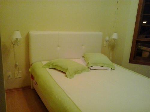 a white bed with two green pillows on it at Apartamento Solar do Centro - Gramado RS in Gramado