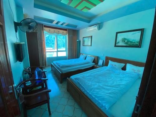 a blue bedroom with two beds and a table and a lamp at Đồng Văn Hotel in Dồng Văn
