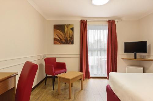a hotel room with a bed and two red chairs at Days Inn Hotel Leicester in Leicester