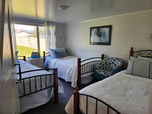 a bedroom with two beds and a chair and a window at #40 Below in Waitarere