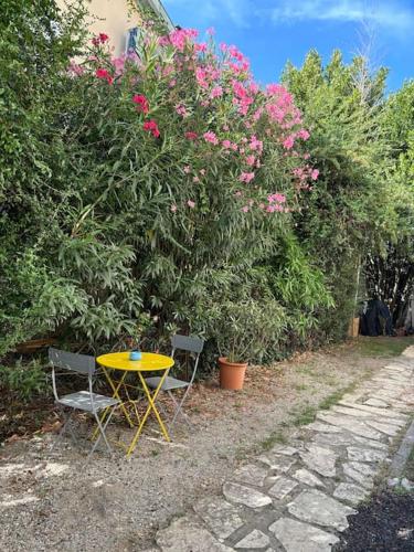 une table et des chaises jaunes à côté d'une brousse avec des fleurs roses dans l'établissement Le Nid Bleu, cœur des Minimes, à Toulouse