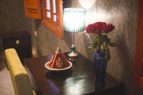 a table with a lamp and a vase of red roses at Riad Andalib in Fès