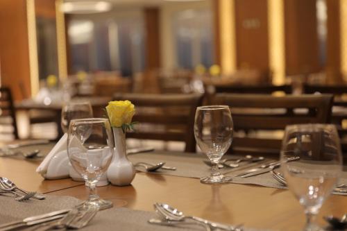a table with glasses and a yellow flower in a vase at Coral Karbala Hotel in Karbalāʼ