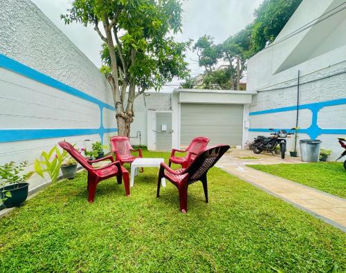 three red chairs and a table in the grass at Sea Breeze Guest House Negombo in Negombo