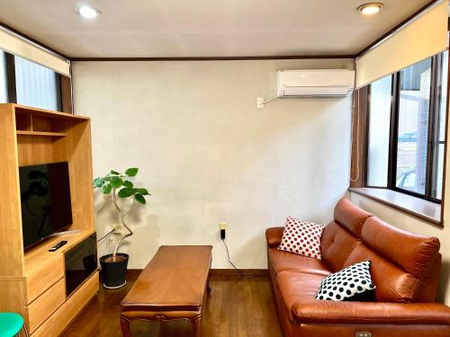 a living room with a leather couch and a table at SUMITSUGU HOUSE Station スミツグハウス ステーション in Kumamoto