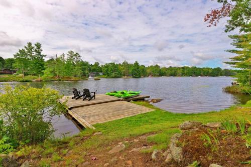 a dock with two chairs and a boat on a lake at Muskoka Retreat, Fire Pit, Games, Waterfront in Gravenhurst