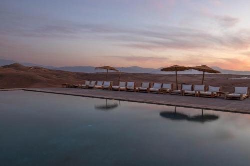 a group of chairs and umbrellas sitting on a pool of water at Alkamar Camp Agafay in El Karia