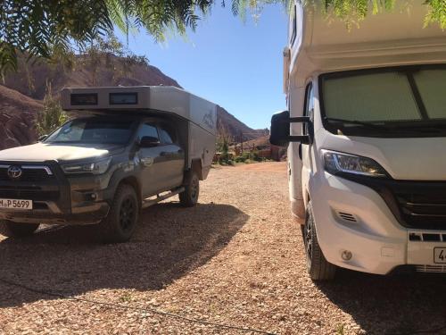 a truck parked next to a camper on a dirt road at Camping Restaurant Pattes des singes in Aït Ougliff