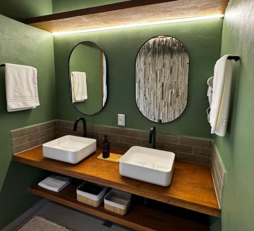 a green bathroom with two sinks and two mirrors at Chalé Mezanela in Pirenópolis