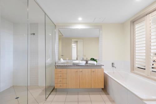 a bathroom with a sink and a tub and a mirror at Golfer's Paradise - Pelican Waters in Pelican Waters