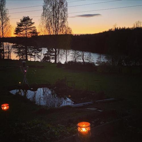 a sunset over a pond with candles in a yard at Sjöutsikt, Röd trästuga med traditionellt yttre Skandinavisk, modernt inre och alla bekvämligheter, Sol hela dagen på stora altanen, Tryggt, Vinterbonat, Fiske, Båt in Skinnskatteberg