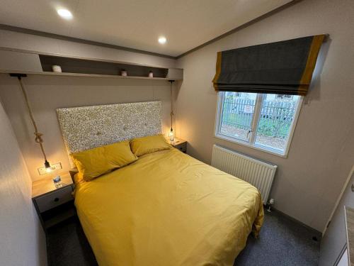 a bedroom with a bed with yellow sheets and a window at Golden Palm Resort - The Stonewood - Coastal Caravan Breaks in Chapel Saint Leonards