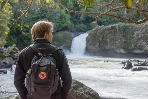 a man with a backpack standing in front of a waterfall at Hotel Termas Puyehue Wellness & Spa Resort in Puyehue