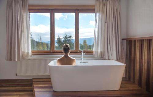 a woman sitting in a bath tub in front of a window at Hotel Termas Puyehue Wellness & Spa Resort in Puyehue