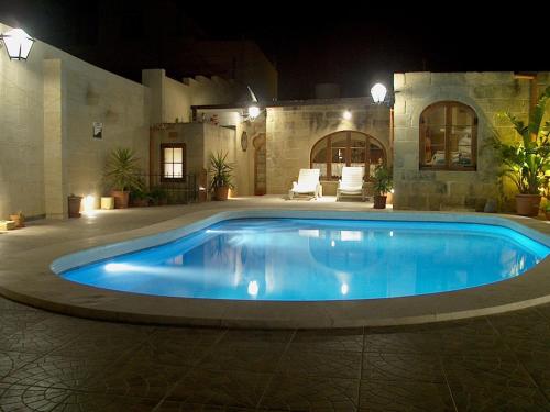 a large blue swimming pool in a yard at night at Barumbara Farmhouse in Sannat