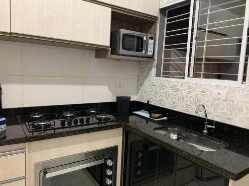 a kitchen with a stove and a sink and a microwave at Aconchego Dutra in Praia Grande
