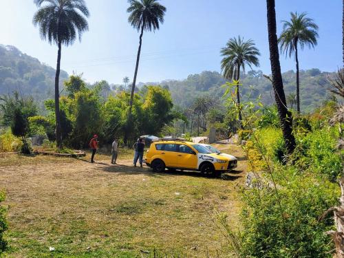 a yellow car parked on a dirt road with palm trees at Valley Nest for 6-12 PAX in Mount Ābu