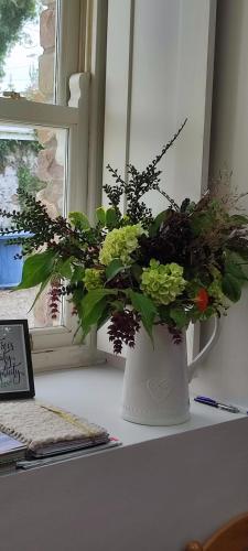 a white vase with flowers on a desk next to a window at The Old House at Belfield in Tralee