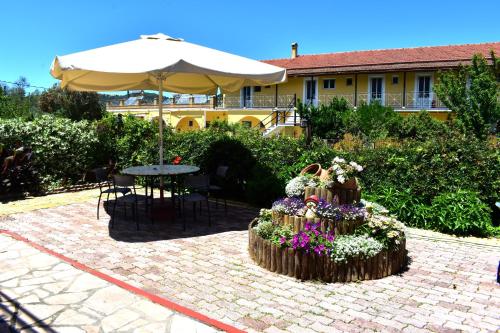 a patio with a table and an umbrella and flowers at Kostas Apartments & studios in Agios Georgios Pagon