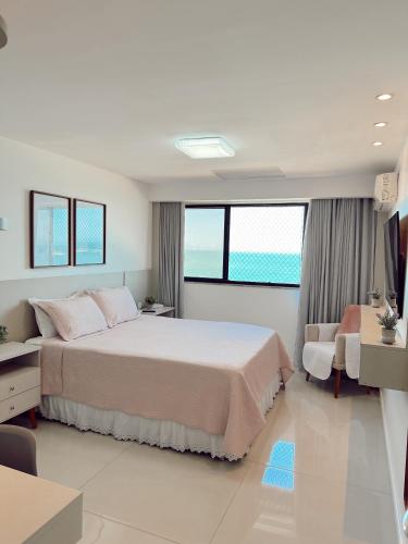 a white bedroom with a large bed and a chair at Praia da Costa, SUNRISE STAY in Vila Velha