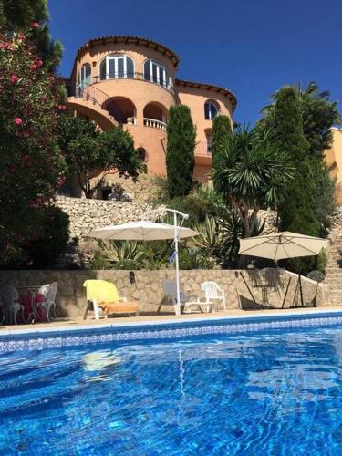 a swimming pool with chairs and umbrellas in front of a building at Havre de Montemar Vue et Piscine in Benissa