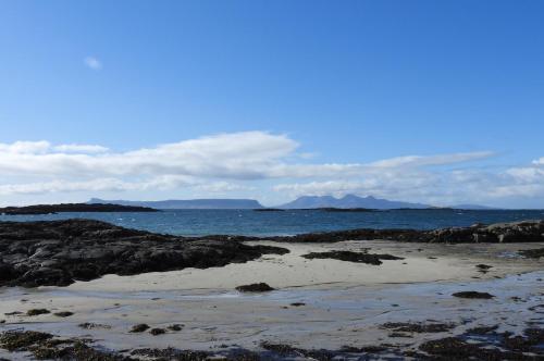 a beach with rocks and the ocean with mountains in the background at The Wee Lodge in Mallaig
