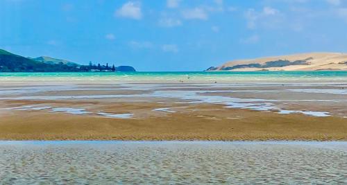 a beach with the ocean and mountains in the background at 'Noni's House' Coastal Opononi Hokianga in Opononi