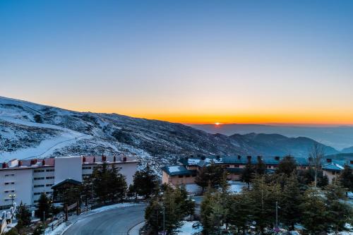 a building on a mountain with the sunset in the background at Apartamentos Boabdil in Sierra Nevada