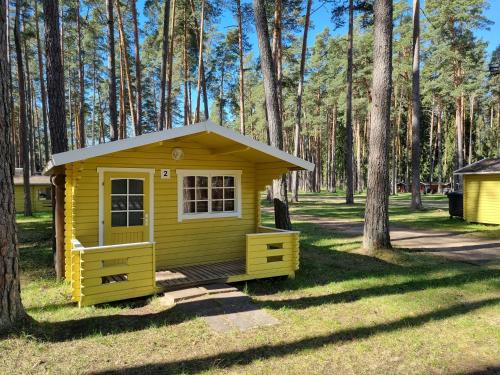 a small yellow cabin in the grass with trees at Tartumaa Tervisespordikeskus in Uderna
