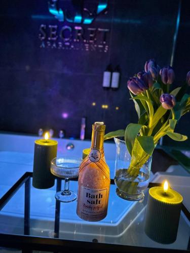 a glass table with a bottle and a vase of flowers at Make Love Apartament by Secret Apartament in Toruń