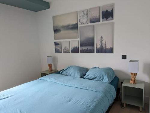 a bedroom with a bed with blue sheets and pictures on the wall at Rez de jardin proche mer in Arradon
