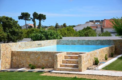 a swimming pool with a stone retaining wall and a stone retaining wall at Tree House - Casa Laranjeira in Quinta do Conde