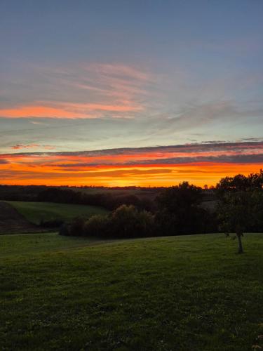 a sunset over a field with a tree in a field at La Grange du Bois des Arrendies in La Salvetat-Belmontet