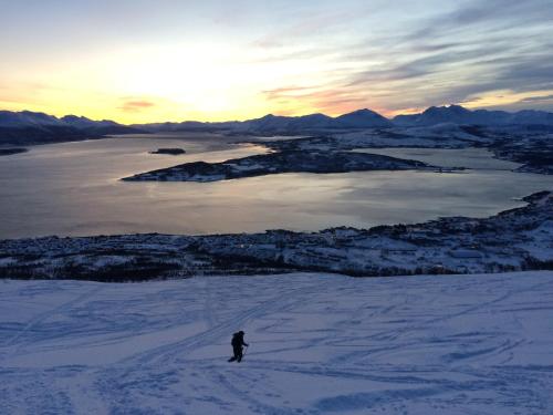 a person skiing down a snow covered slope with the sunset at Eide Aurora Apartement in Tromsø